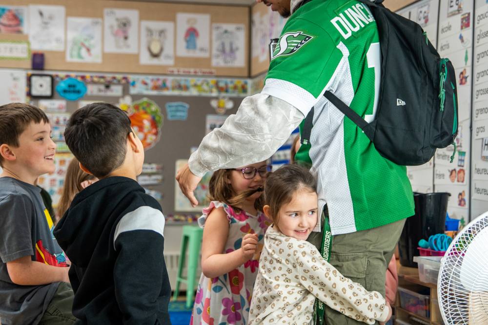 Young students hugging a Roughriders player in their classroom